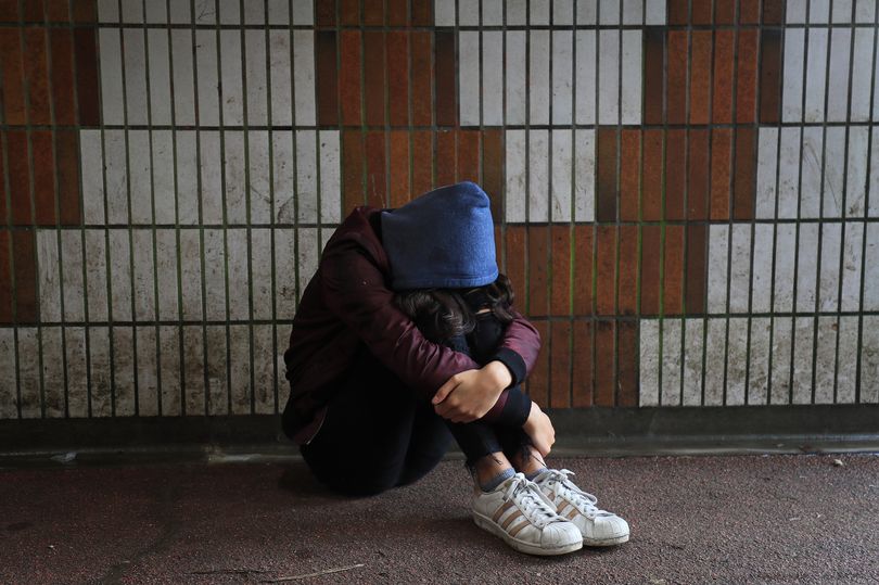 A young man sitting on a dirty subway street looking desperate