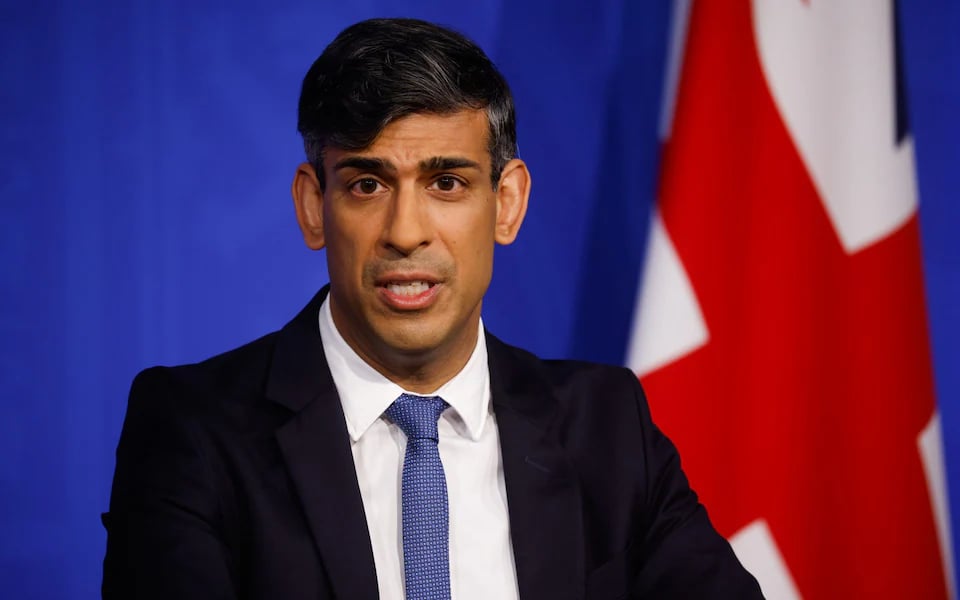 Rishi Sunak mid-sentence standing in front of a Union Jack flag